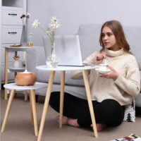 Frau sitzt auf dem Boden vor einer Couch und nutzt das 2er-Set runder Beistelltische als Laptop- und Kaffeetisch. Gemütliche Wohnatmosphäre mit minimalistischer Einrichtung.