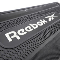 Nahaufnahme des Reebok-Logos auf der Oberfläche eines Stepbretts. Das strukturierte Design mit weißer Schrift hebt sich deutlich vom schwarzen Hintergrund ab.